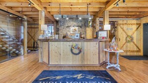 A wooden reception desk with a stone wall backdrop, a small table with a vase, and a welcome sign. - Empty Arms Parlor - Rm. 208 (Stanardsville)