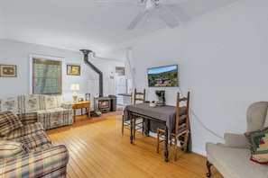 A cozy living room with a fireplace, wooden flooring, and a dining area with a table and chairs. - Bear Paw Mountain Cottage (Stanardsville)