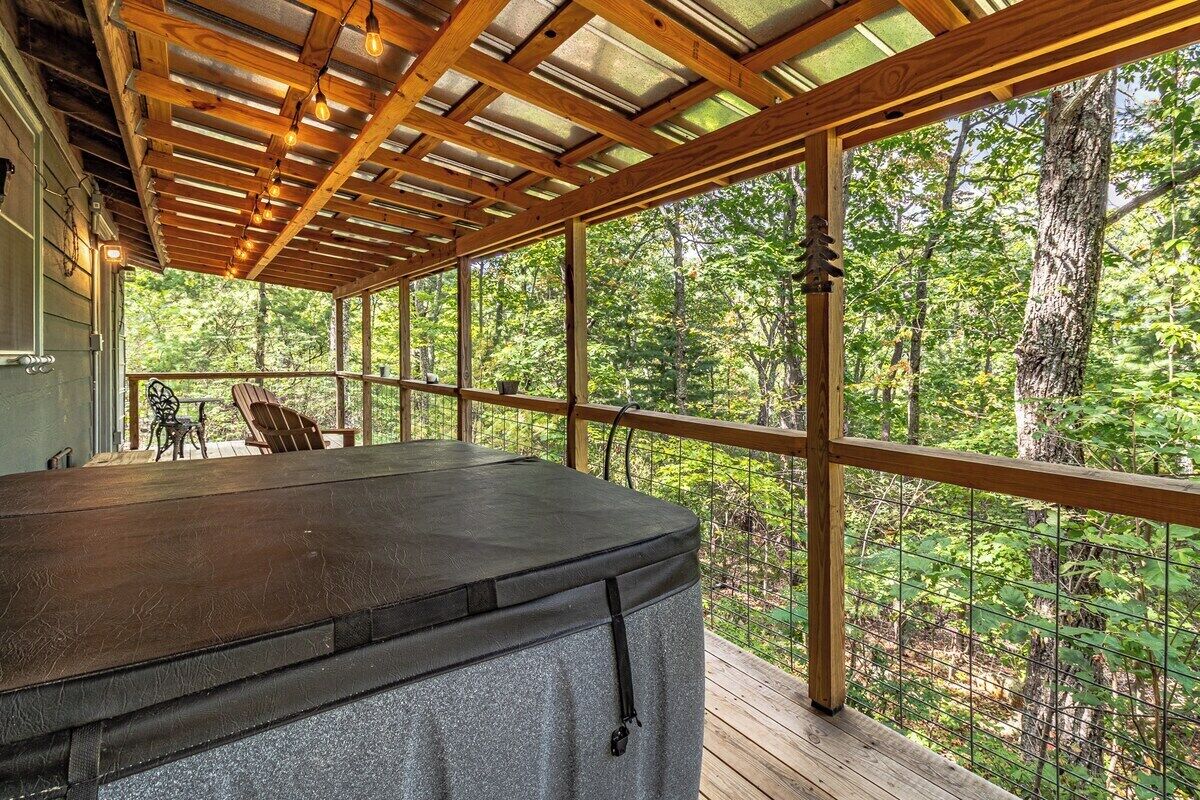 A covered outdoor deck with a hot tub, wooden beams, and a view of the forest.