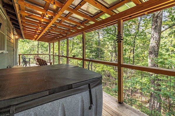 A covered outdoor deck with a hot tub, wooden beams, and a view of the forest. - Bear Paw Mountain Cottage (Stanardsville)