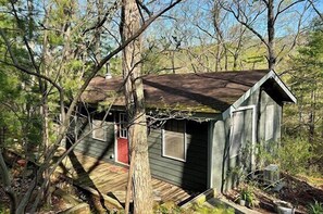 A small, rustic cabin with a wooden exterior, a red door, and a sloped roof surrounded by trees.