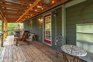 A wooden deck with a table and chairs, a red door, and a window with a view of trees. - Bear Paw Mountain Cottage (Stanardsville)