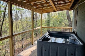 A hot tub in a covered outdoor area with a wooden deck and a view of the surrounding forest. - Bear Paw Mountain Cottage (Stanardsville)