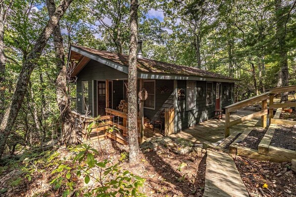 A rustic cabin with a wooden deck, surrounded by trees. - Bear Paw Mountain Cottage (Stanardsville)