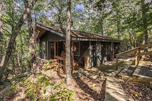 A rustic cabin with a wooden deck, surrounded by trees. - Bear Paw Mountain Cottage (Stanardsville)