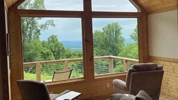 Eine Holzhütte mit großem Fenster, einem Balkon und zwei Stühlen.
