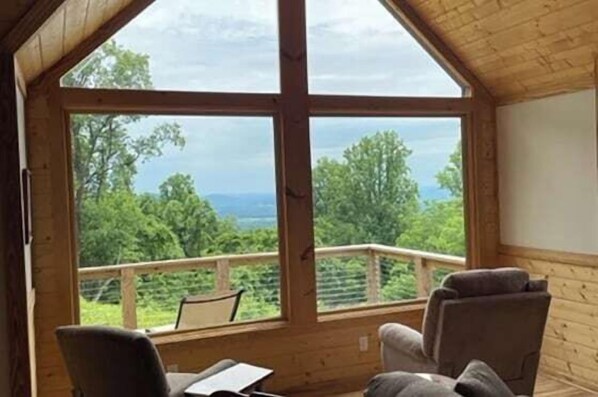 A wooden cabin with a large window, a balcony, and two chairs.