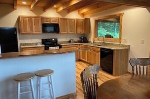 A kitchen with wooden cabinets, a microwave, a stove, and a sink. There are two stools and a dining table with chairs.