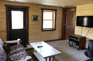 A room with a wooden door, a window, a television mounted on the wall, a sofa, and a table.
