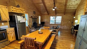 A wooden cabin interior with a dining table, benches, a refrigerator, a fireplace, and a television. - Southern Comfort Cabin (Stanardsville)
