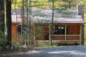 A wooden cabin with a porch, surrounded by trees.