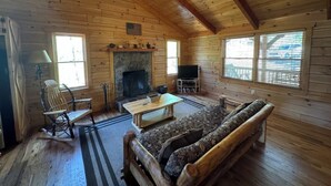 A log cabin interior with a fireplace, wooden furniture, and a television. - Southern Comfort Cabin (Stanardsville)