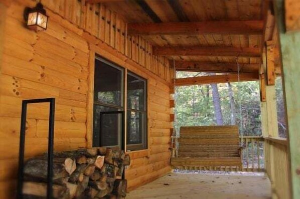 A wooden cabin with a porch, a bench, and a stack of firewood.