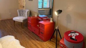 A room with a wooden floor, a red dresser, a chair, a mirror, and a lamp. - Hollywood Suite - Rm. 204 (Stanardsville)