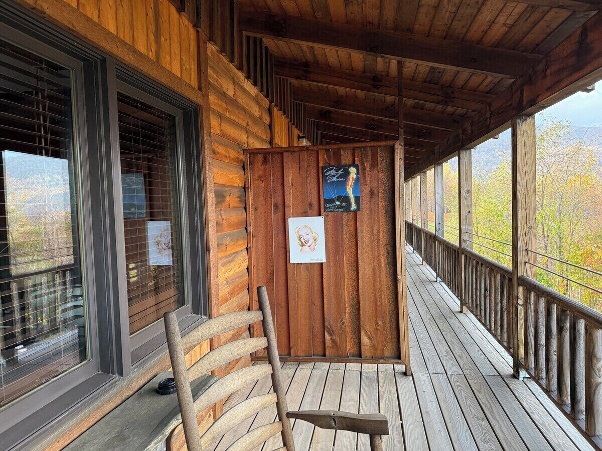 Una cabaña de madera con un porche, una mecedora y vistas a árboles otoñales.