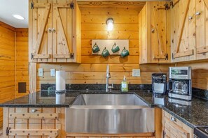 A kitchen with wooden cabinets, a stainless steel sink, a coffee maker, and a wall-mounted light fixture. - Mountain Mist Mountain Cabin (Stanardsville)