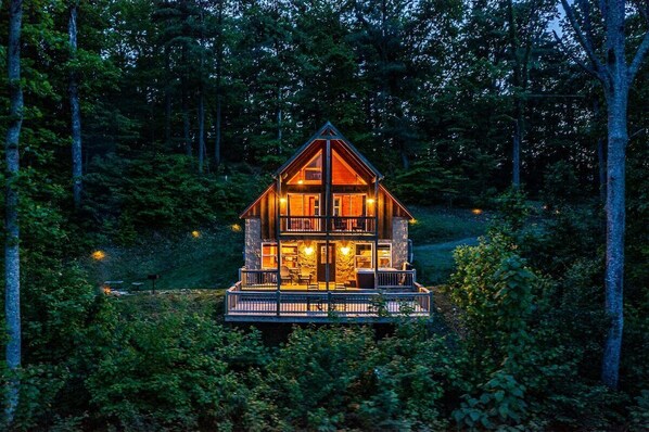 A cabin with a balcony, large windows, and a stone exterior.
