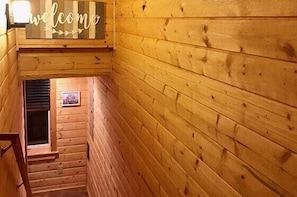 Interior de madera con un cartel de 'welcome', una escalera y un cuadro en la pared.