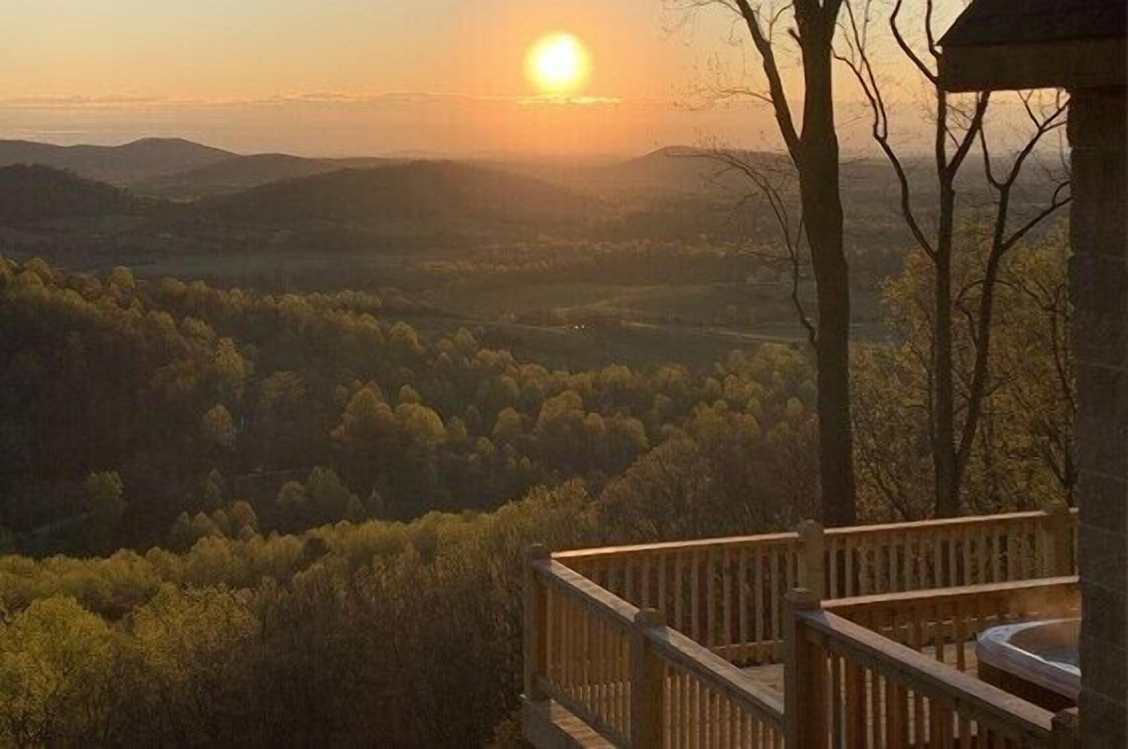 A sunset view from a wooden deck overlooking a forested valley.