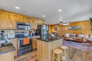A kitchen with wooden cabinets, stainless steel appliances, and a central island with stools. - Mountain Mist Mountain Cabin (Stanardsville)