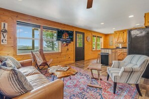 A cozy cabin interior with a wooden exterior, a living room with a sofa and armchairs, a dining area, and a kitchen.