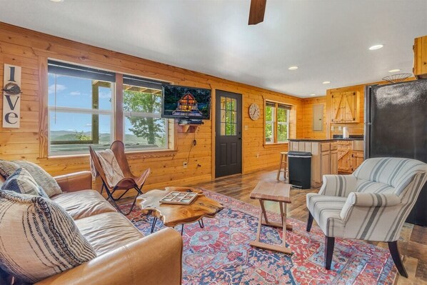 A cozy cabin interior with a wooden exterior, a living room with a sofa and armchairs, a dining area, and a kitchen. - Mountain Mist Mountain Cabin (Stanardsville)