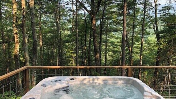 Un jacuzzi rodeado por una terraza de madera y una zona boscosa.