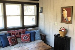 A room with a sofa, pillows, a window, a wall-mounted picture, and a cabinet.