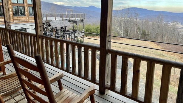 A wooden deck with chairs, a table, and a view of mountains.