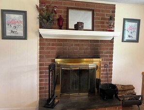A fireplace with a brick wall, a mantel with decorative items, and framed pictures on the wall. - Mountain View Farmhouse (Stanardsville)