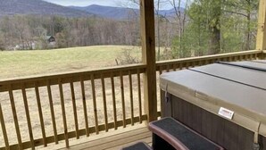 Une terrasse dotée d’un jacuzzi, de rampes en bois et offrant une vue sur un champ verdoyant et des montagnes.