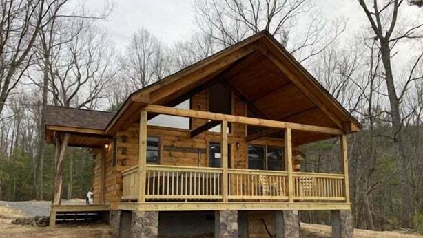 Une cabane en bois dotée d’un balcon, de grandes fenêtres et de fondations en pierre.