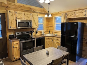 A wooden cabin-style kitchen with a stove, microwave, refrigerator, and wooden cabinets.