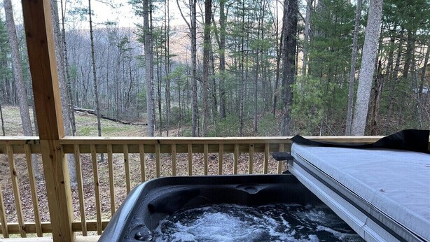 Een hottub op een houten terras met uitzicht op een bos.