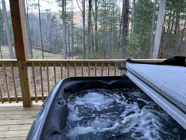 A hot tub on a wooden deck with a forest view.