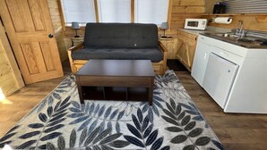 A cozy cabin interior with a sofa, a small table, a kitchen area with a microwave, and a refrigerator. - Bamboo Beetle Cabin Pod (Stanardsville)
