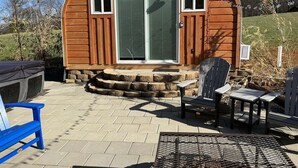 A wooden cabin with a large sliding glass door, outdoor seating, and a stone staircase leading to the entrance. - Bamboo Beetle Cabin Pod (Stanardsville)
