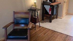 Una sedia di legno con seduta imbottita, un piccolo tavolino rotondo con una lampada e un estintore su un mobiletto in legno.