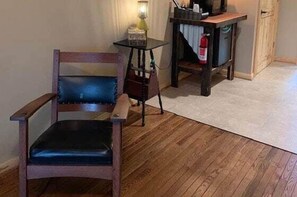 A wooden chair with a cushioned seat, a small round table with a lamp, and a fire extinguisher on a wooden cabinet. - Black Smith - Rm. 106 (Stanardsville)