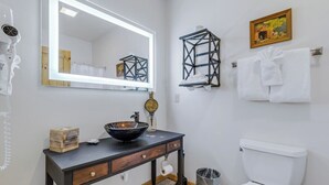 Un bagno con un lavandino moderno, un water, uno specchio con illuminazione e un porta asciugamani.
