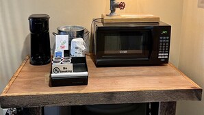 Angolo cottura con macchina del caffè, forno a microonde e una sveglia appesa al muro.