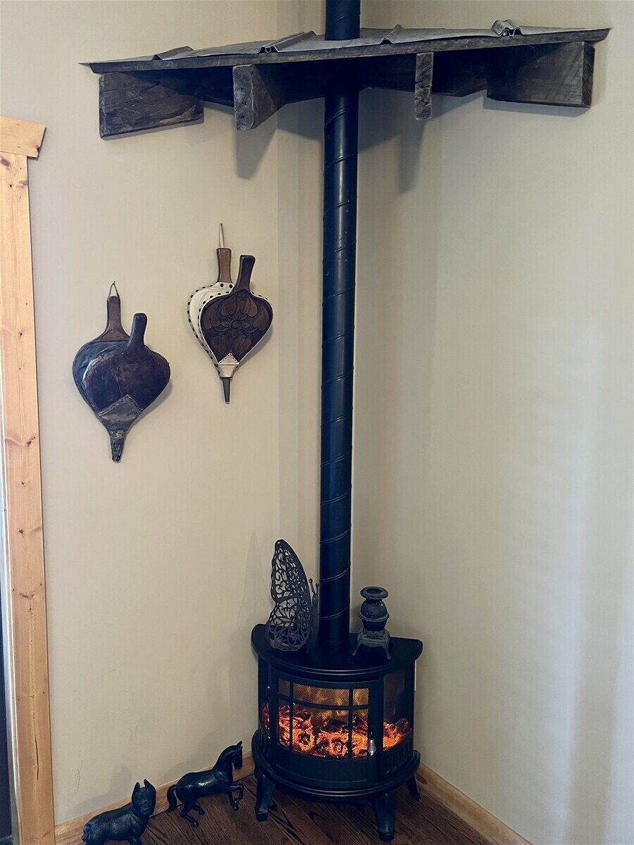 Habitación de esquina con un estufa de leña de madera negra, un estante de madera y dos elementos decorativos colgantes.