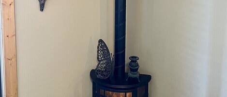 Habitación de esquina con un estufa de leña de madera negra, un estante de madera y dos elementos decorativos colgantes.