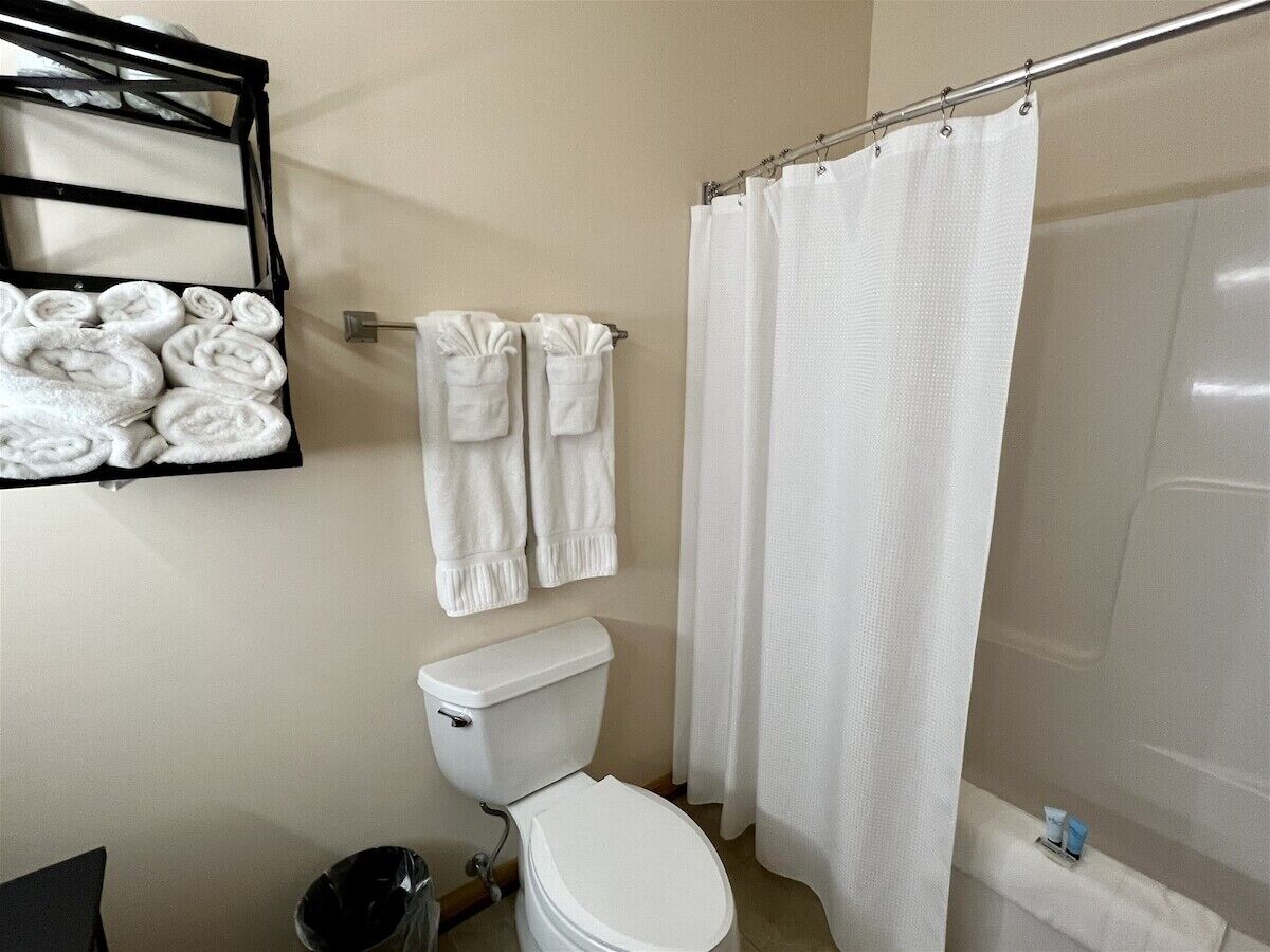 A bathroom with a toilet, a shower curtain, and a rack with rolled towels.