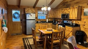A wooden cabin interior with a kitchen, dining area, and a door leading outside. - Sweet Reunion Mountain Cabin (Stanardsville)