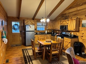 A wooden cabin interior with a kitchen, dining area, and a door leading outside. - Sweet Reunion Mountain Cabin (Stanardsville)