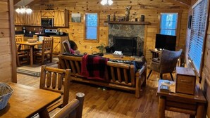 A log cabin interior with a dining area, a fireplace, a kitchen, and a living room with a sofa and chairs. - Sweet Reunion Mountain Cabin (Stanardsville)