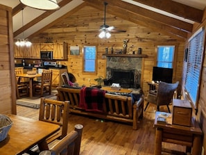 A log cabin interior with a dining area, a fireplace, a kitchen, and a living room with a sofa and chairs. - Sweet Reunion Mountain Cabin (Stanardsville)