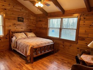 Une chambre dans une cabane en bois, avec un lit, un ventilateur de plafond et une fenêtre équipée de stores.