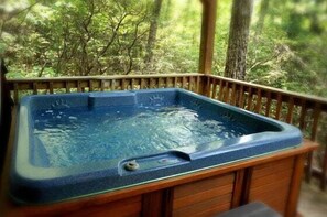 A hot tub on a wooden deck with a forest backdrop.
